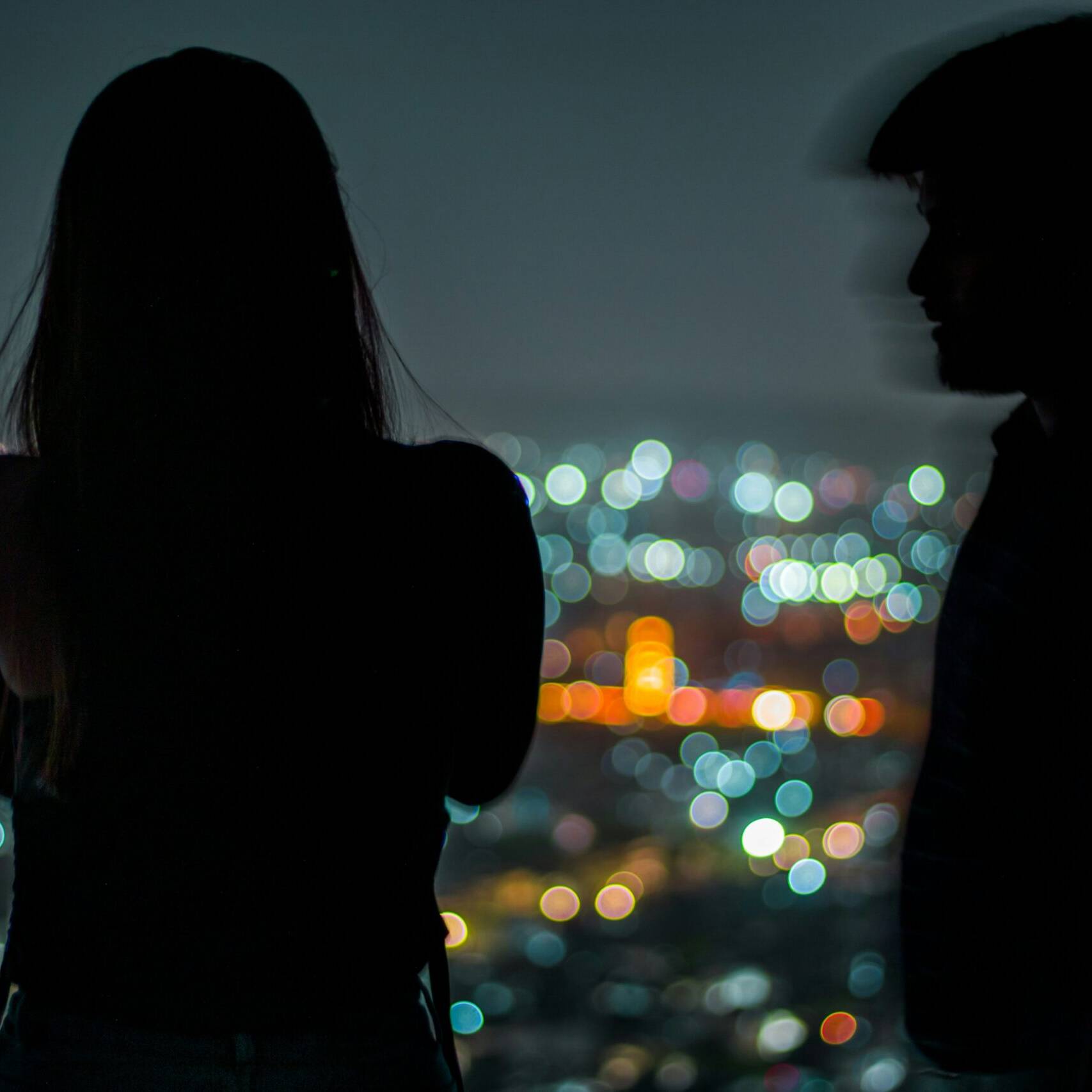 Ein Paar, distanziert, mit einem Blick auf das Lichtermeer eine Gro&szlig;stadt